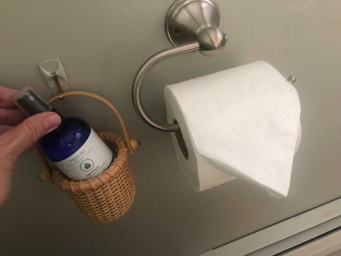 Hand holding spray bottle in a small basket next to a toilet paper roll, illustrating unexpected tools for jobs.