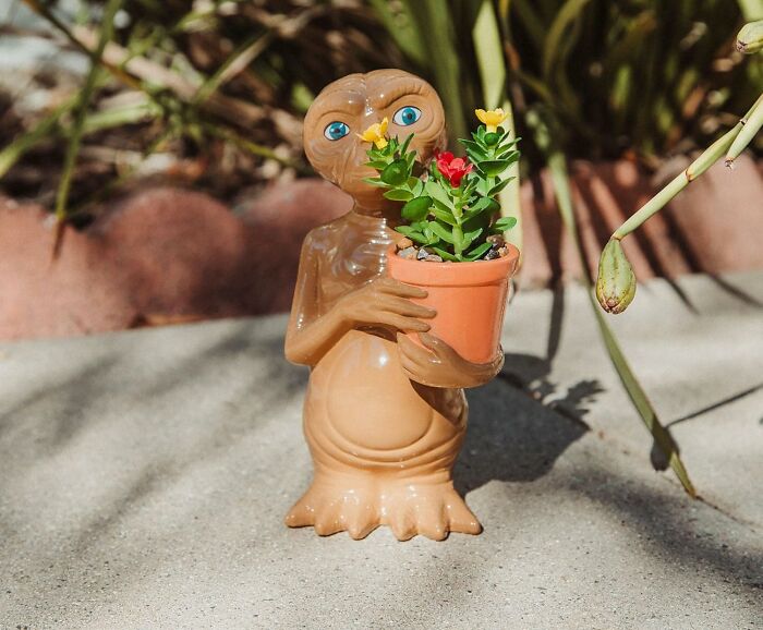 Alien figurine with a flower pot, showcasing pure fandom goals in a garden setting.