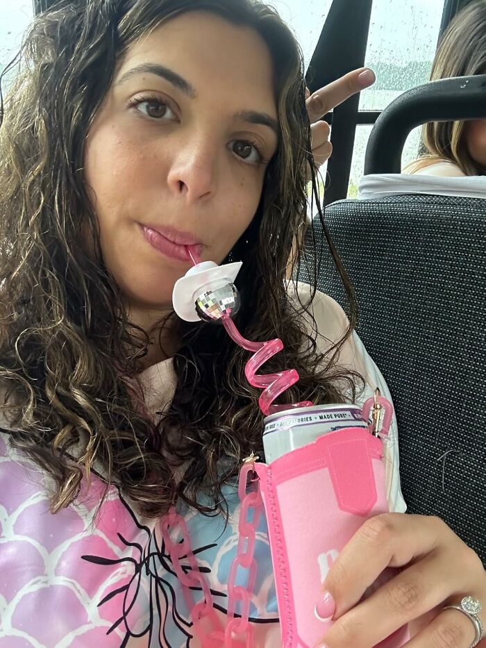 A woman drinks from a can using a curly straw, showing a quirky, unexpected accessory.