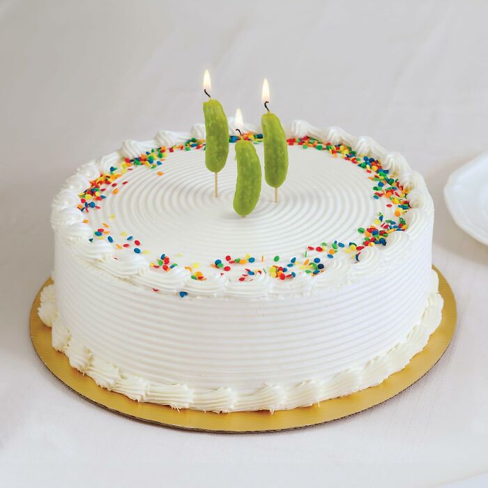 White cake with colorful sprinkles and Genuine Fred pickle candles lit on top.