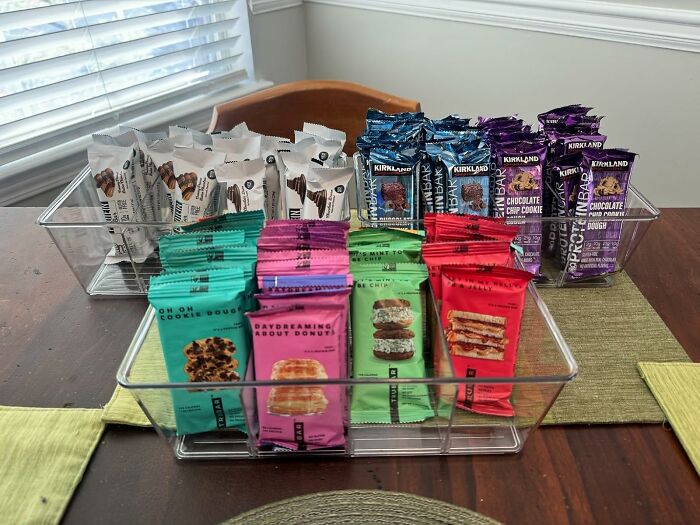 Costco snack packs arranged neatly in clear bins on a dining table.