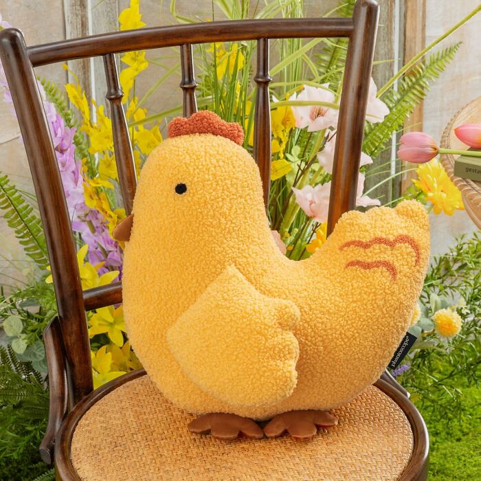 Cute plush chicken on a wooden chair surrounded by colorful flowers.