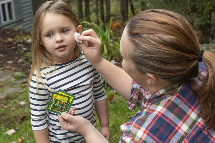 Woman cleaning girl's ear in spring garden using wipes.