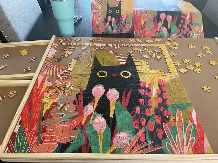Genuine Fred puzzle in progress, featuring a whimsical black cat amid colorful flowers on a table.