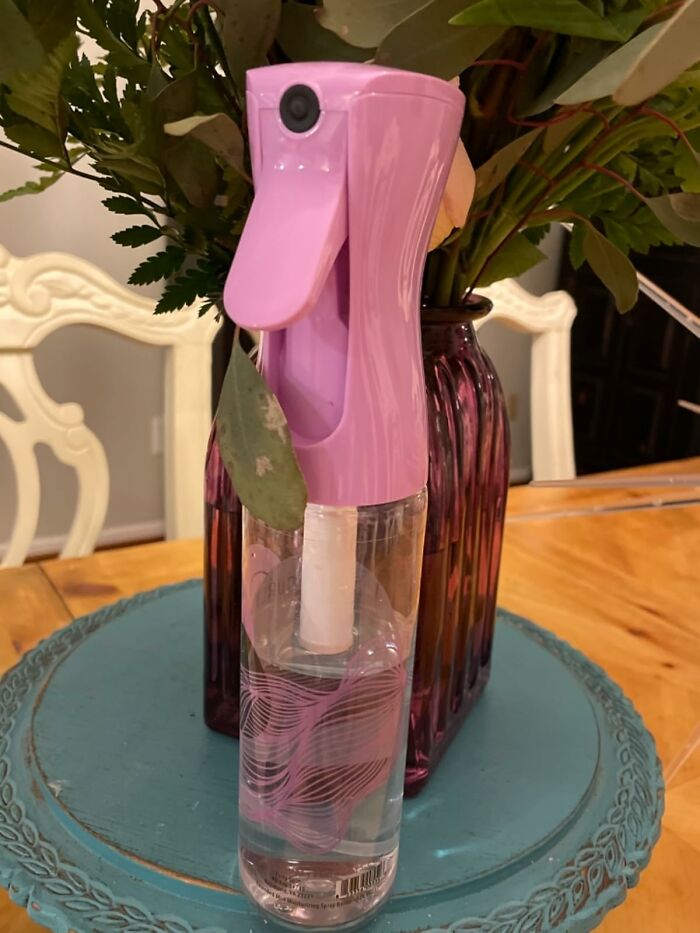 Pink spray bottle on a decorative tray for curly hair care solutions.