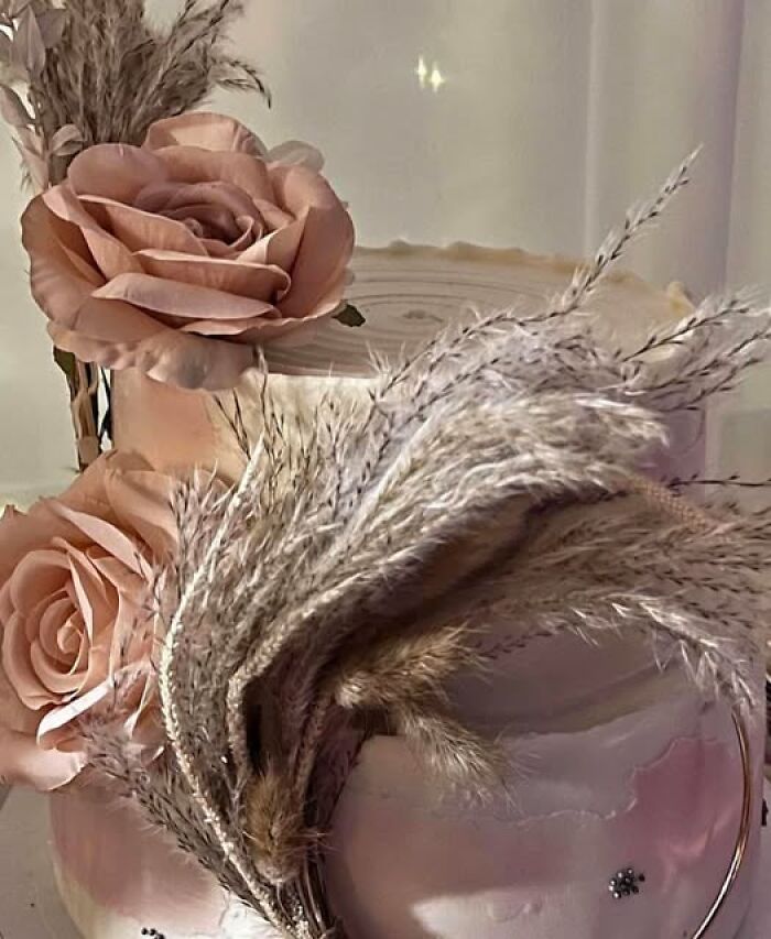 Decorative cake adorned with pink roses and pampas grass, showcasing a whimsical baking creation.