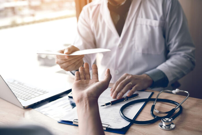 Doctor handing prescription to patient, highlighting normal healthcare practices with medical tools on the desk.