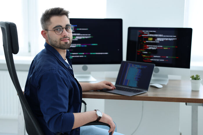 A man with glasses sits at a desk, working on code, showcasing life with a "useless" degree.