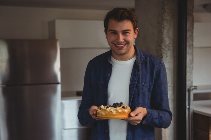 Man in a denim shirt holding a cake, smiling warmly, a possible green flag on a first date.