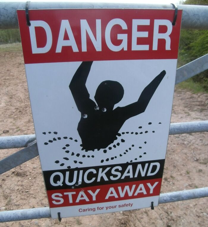 Quicksand danger sign on a metal gate with graphic of a person sinking, emphasizing safety warnings.