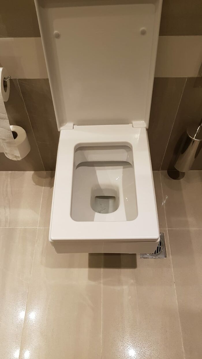 Modern white wall-mounted toilet in a bathroom featuring beige tiles, showcasing poorly-aging interior design trends.