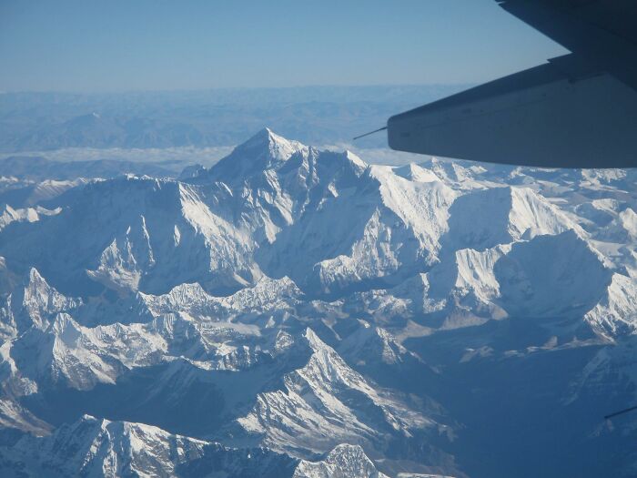 Awe-inspiring view of iconic Mount Everest from airplane, showcasing snow-covered peaks and clear skies.