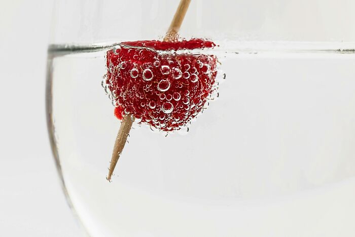 Red raspberry on a toothpick with bubbles in sparkling water.