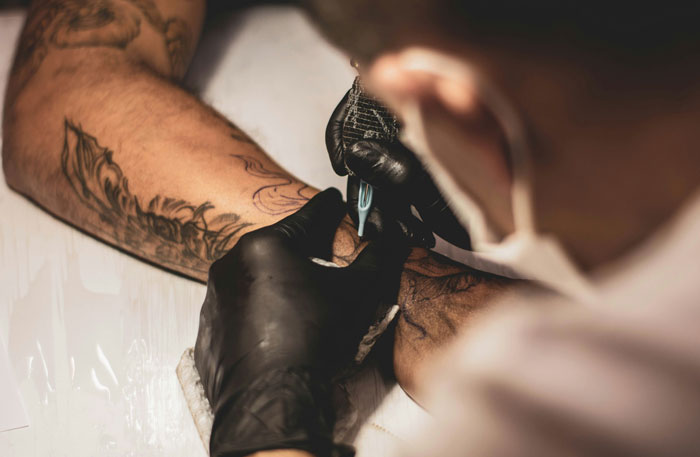 Tattoo artist inking floral design on an arm, focusing on tattoo attractiveness and detail.