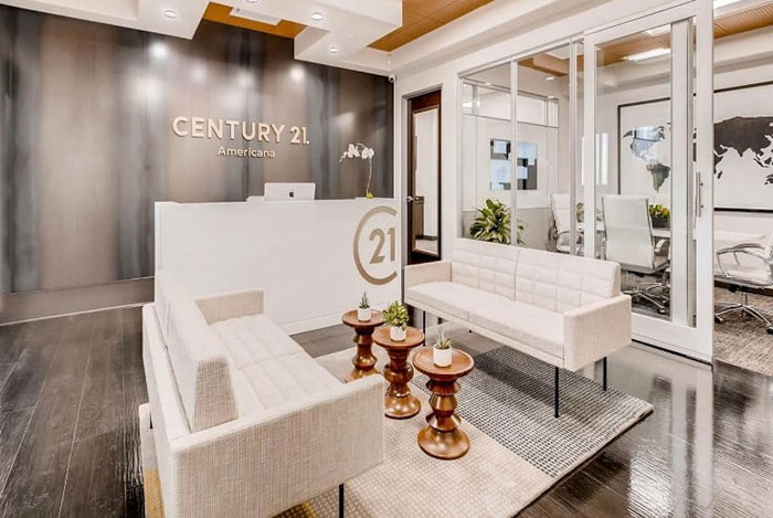 Real estate office lobby with modern furniture, featuring the Century 21 logo on the wall.