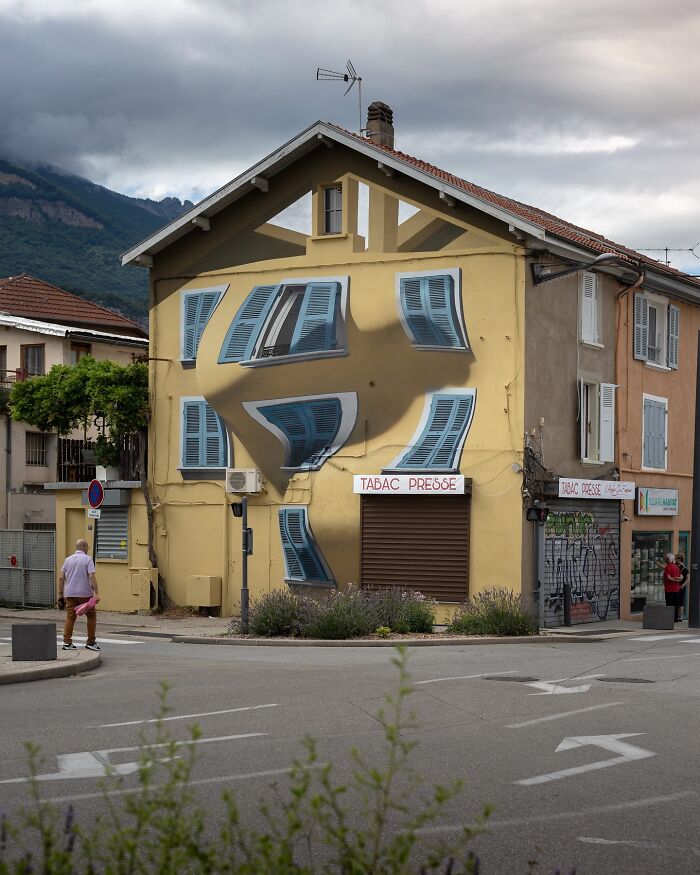 Mind-bending 3D street art creates an optical illusion on a building's facade, transforming windows into warped shapes.