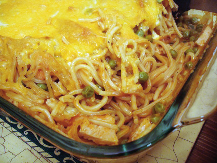 Cheesy spaghetti casserole with peas in glass dish, an example of old-school delicacies.