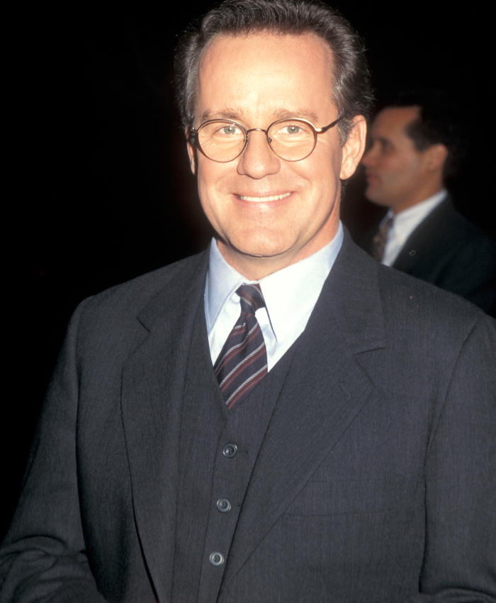 Smiling man in glasses and a suit at a Hollywood event.