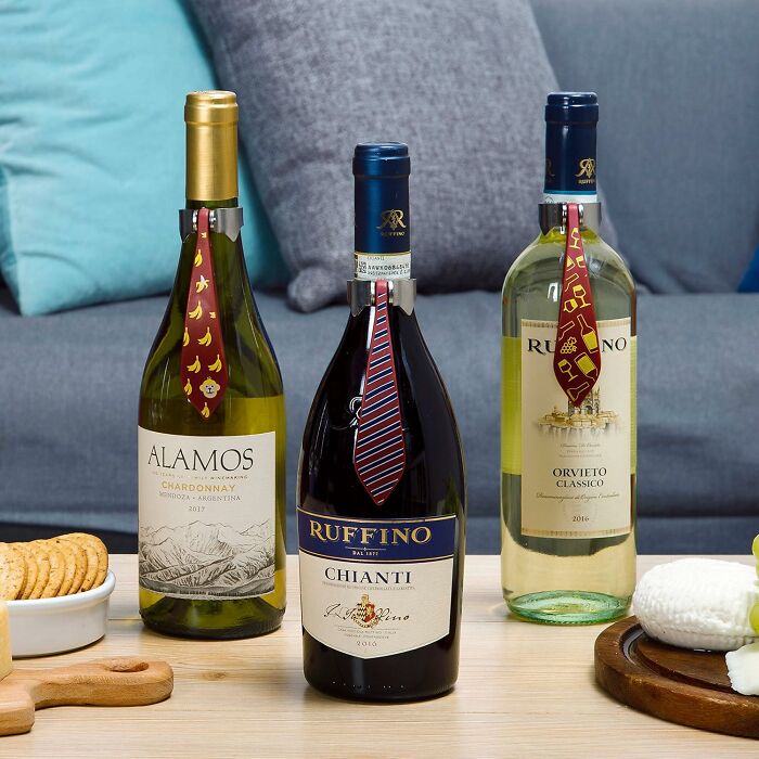 Three wine bottles with novelty ties from Peleg Design Shop on a table with snacks in a cozy setting.
