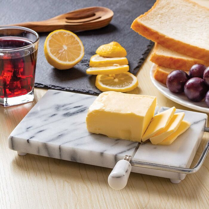 Marble butter slicer with sliced butter alongside lemons, grapes, and toast.
