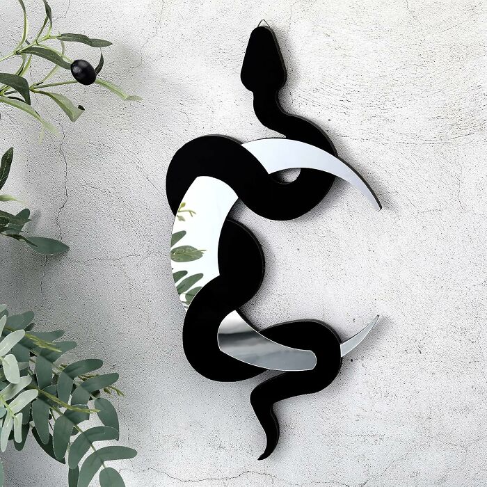 Snake-shaped decorative mirror reflecting greenery on a textured wall, testing our self-control in style.