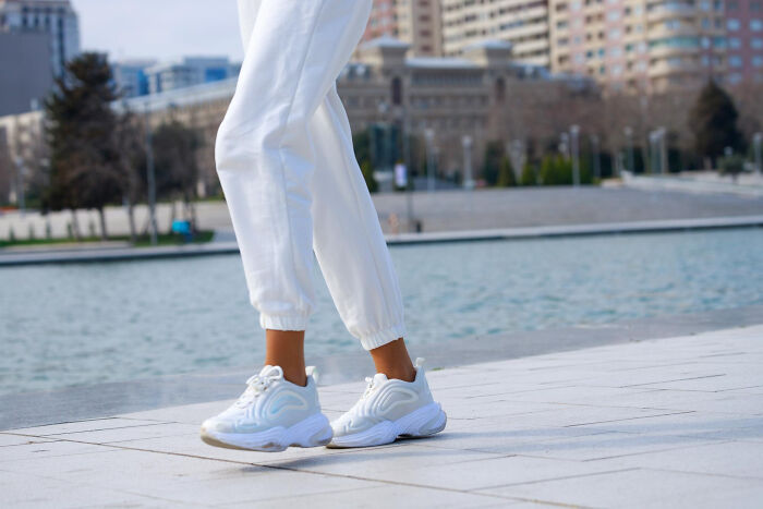 Woman in white pants and sneakers walking outdoors near a city water feature, embodying a relaxed lifestyle.