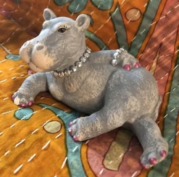 Thrifted hippo figurine adorned with jewelry on a colorful quilted background.