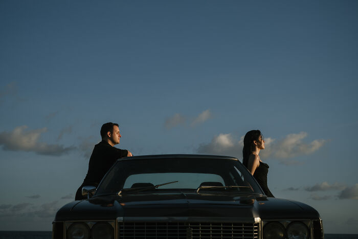 Couple posing on a classic car at sunset, highlighting best engagement photos of 2025 with dramatic sky backdrop.