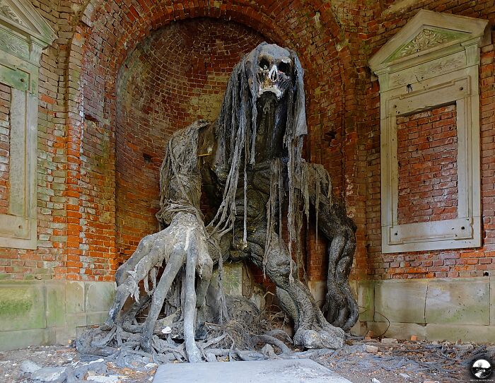 Eerie abandoned place with a large, imposing stone creature in a dilapidated brick alcove.