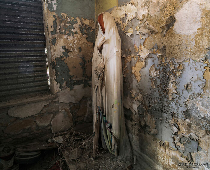 Eerie statue in an abandoned building corner with peeling paint and debris.