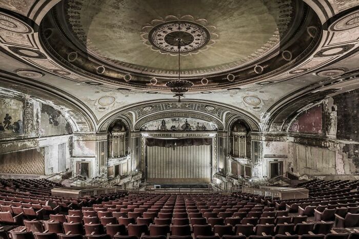 Eerie abandoned theater with ornate ceiling and peeling walls, showcasing decayed elegance.
