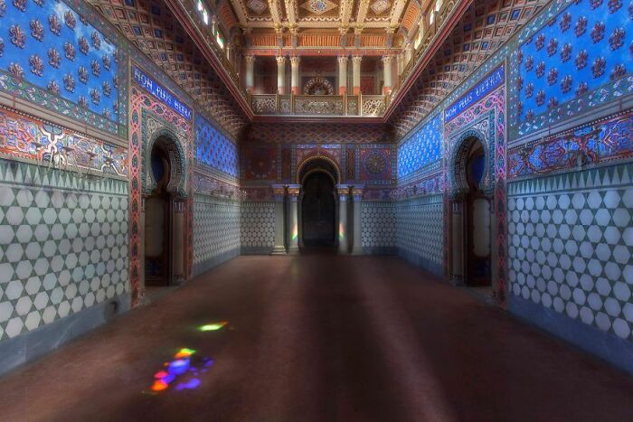 Eerie abandoned place with ornate blue and red walls, arched doorways, and colorful light reflections on the floor.
