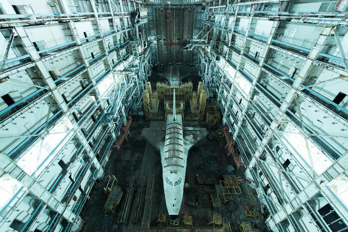 Abandoned spacecraft in a dilapidated hangar, surrounded by rusting scaffolding and machinery.