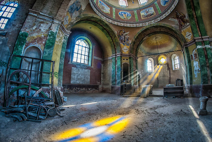 Abandoned church interior with colorful light streaming through stained glass windows, highlighting decay and eerie beauty.