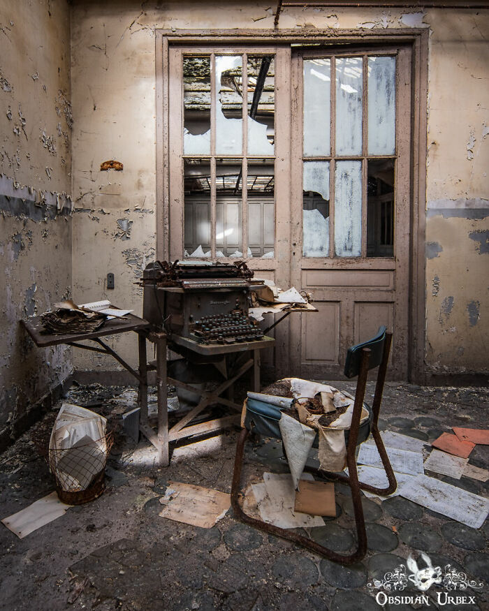 Old typewriter in an eerie abandoned room with peeling walls and scattered papers.
