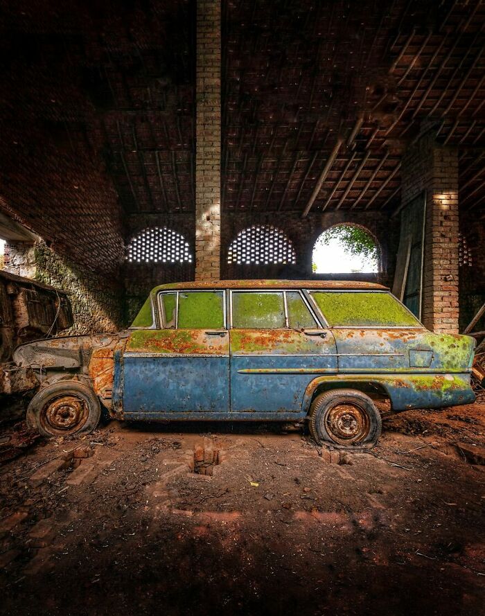 Rusty, abandoned car in an eerie, dimly lit garage.