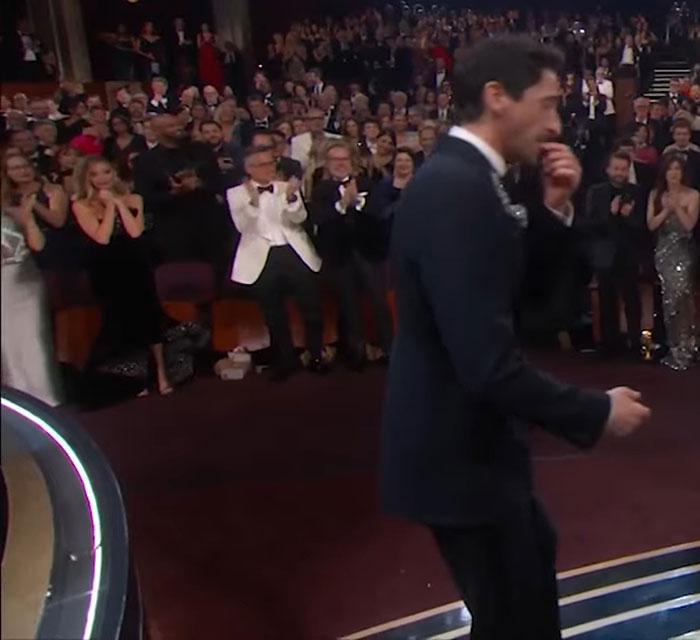 Adrien Brody during his Oscars speech, audience clapping, Cillian Murphy's look going viral in the background.