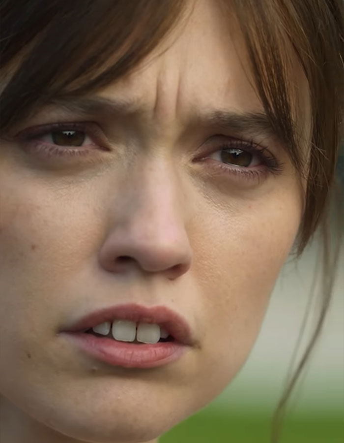 The White Lotus star with a serious expression, close-up focus on teeth.