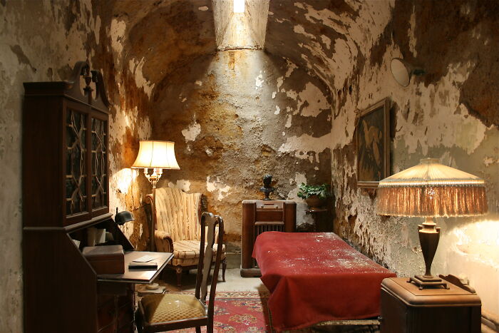A historic cell room with vintage furniture and peeling walls, showcasing iconic place ambiance.