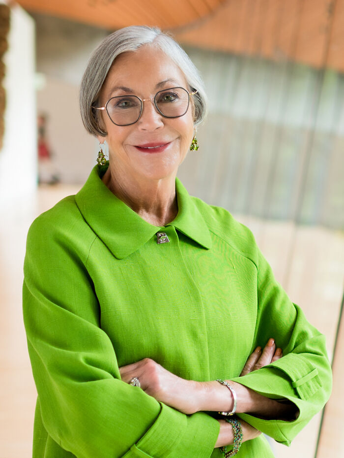 Senior woman in green jacket and glasses standing confidently, related to the richest people and wealth comparison concept.