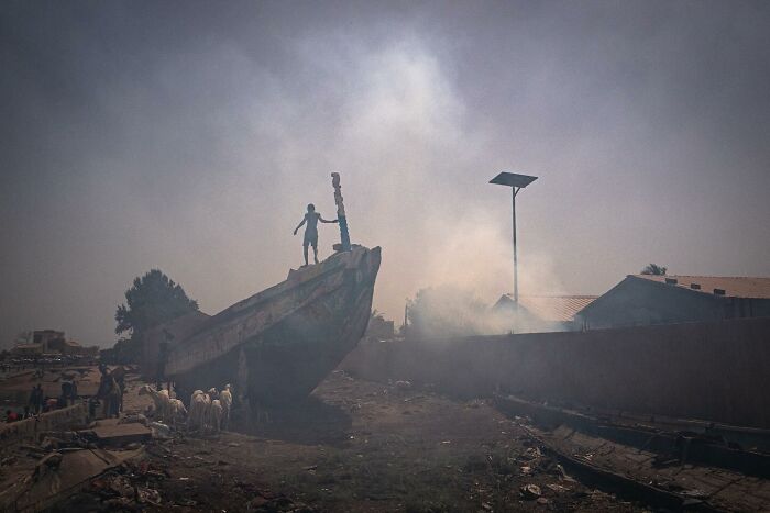 A person stands atop a grounded boat in a smoky street, captured in Andrea Torrei's street photo.