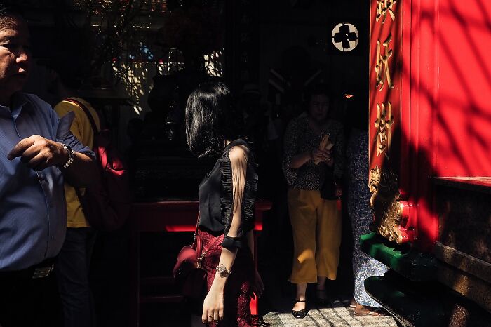 Street photo capturing a woman walking past a vibrant red building with shadows, highlighting Andrea Torrei's curious eye.