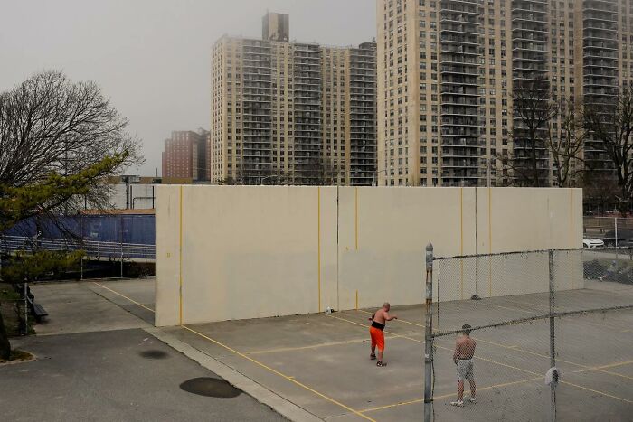 Street photo by Andrea Torrei showing two men playing handball in an urban setting with high-rise buildings in the background.