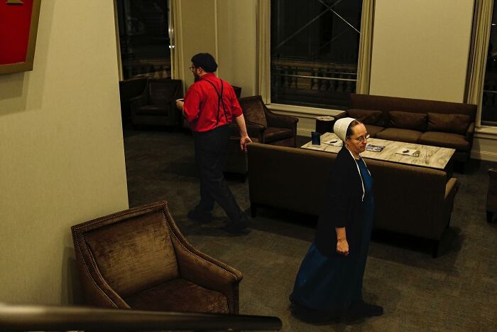 Street photo by Andrea Torrei showing two people in a dimly lit lounge area with chairs and a table.