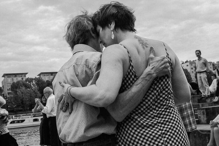 A couple embraces closely in a bustling street scene, captured by Andrea Torrei.