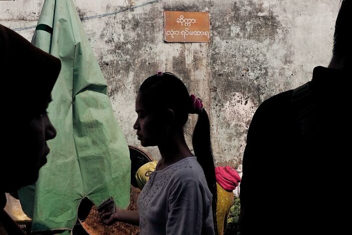 Street photo by Andrea Torrei featuring a woman with a ponytail in profile, holding a phone against an urban backdrop.