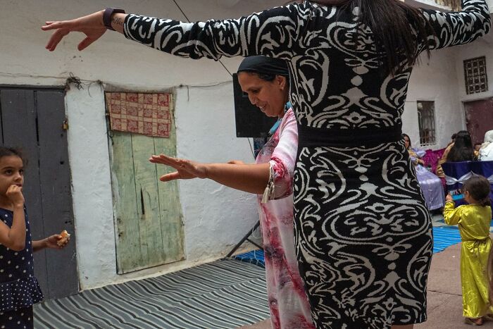 Street photo by Andrea Torrei depicting a lively scene with two women dancing and children nearby.