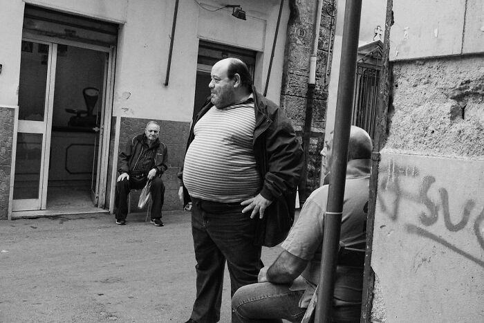 Street photo by Andrea Torrei showing three men in conversation outside a building.