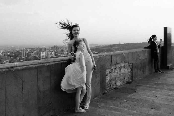 A woman and child enjoy a windy moment on a city overlook, capturing a candid street photo.