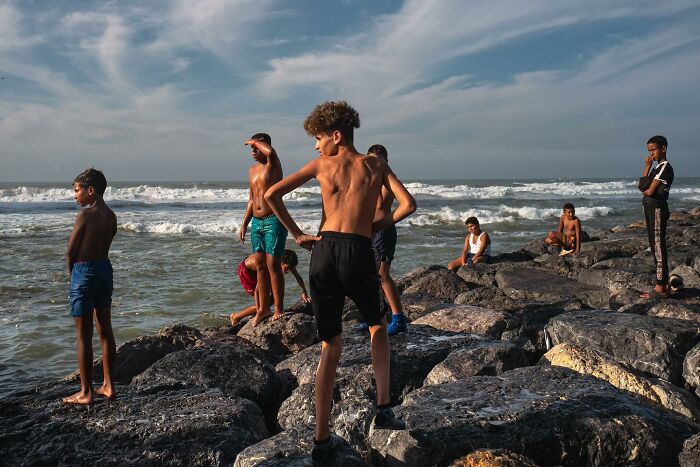 Children on rocky shore under cloudy sky, showcasing street photography by Andrea Torrei.